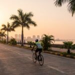 Cyclist riding on Palm Beach Road cycling track in Navi Mumbai during early morning with creek and skyline view