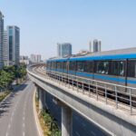 Navi Mumbai Metro train on elevated viaduct passing through modern city with palm trees and residential towers