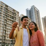 Young couple holding house keys in front of new residential apartment building in Navi Mumbai under PMAY scheme