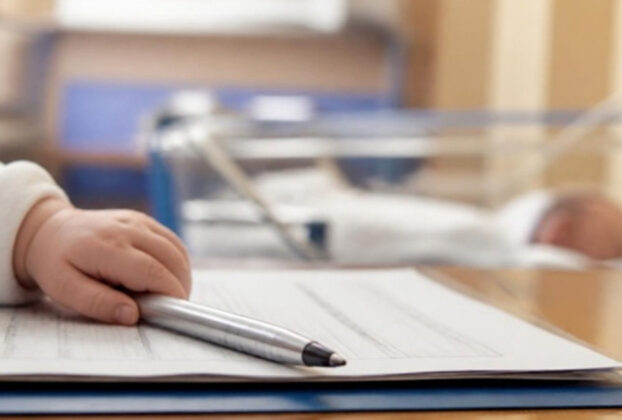 A newborn baby's hand resting on a document with a pen