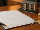 Illustrative image of a property document, keys and a residential building model on a desk. Does not depict an actual document or building.
