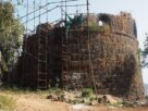 A bastion of Belapur Fort covered in scaffolding with Navi Mumbai buildings behind it