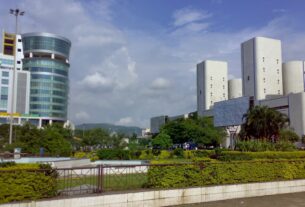 Glass and concrete office towers beside landscaped gardens under a blue sky in Navi Mumbai