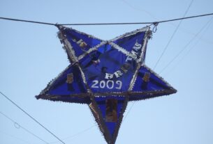 A blue star shaped Christmas lantern hanging from a wire against a pale sky in Mumbai