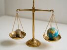 A brass balance scale with coins on one pan and a small globe on the other