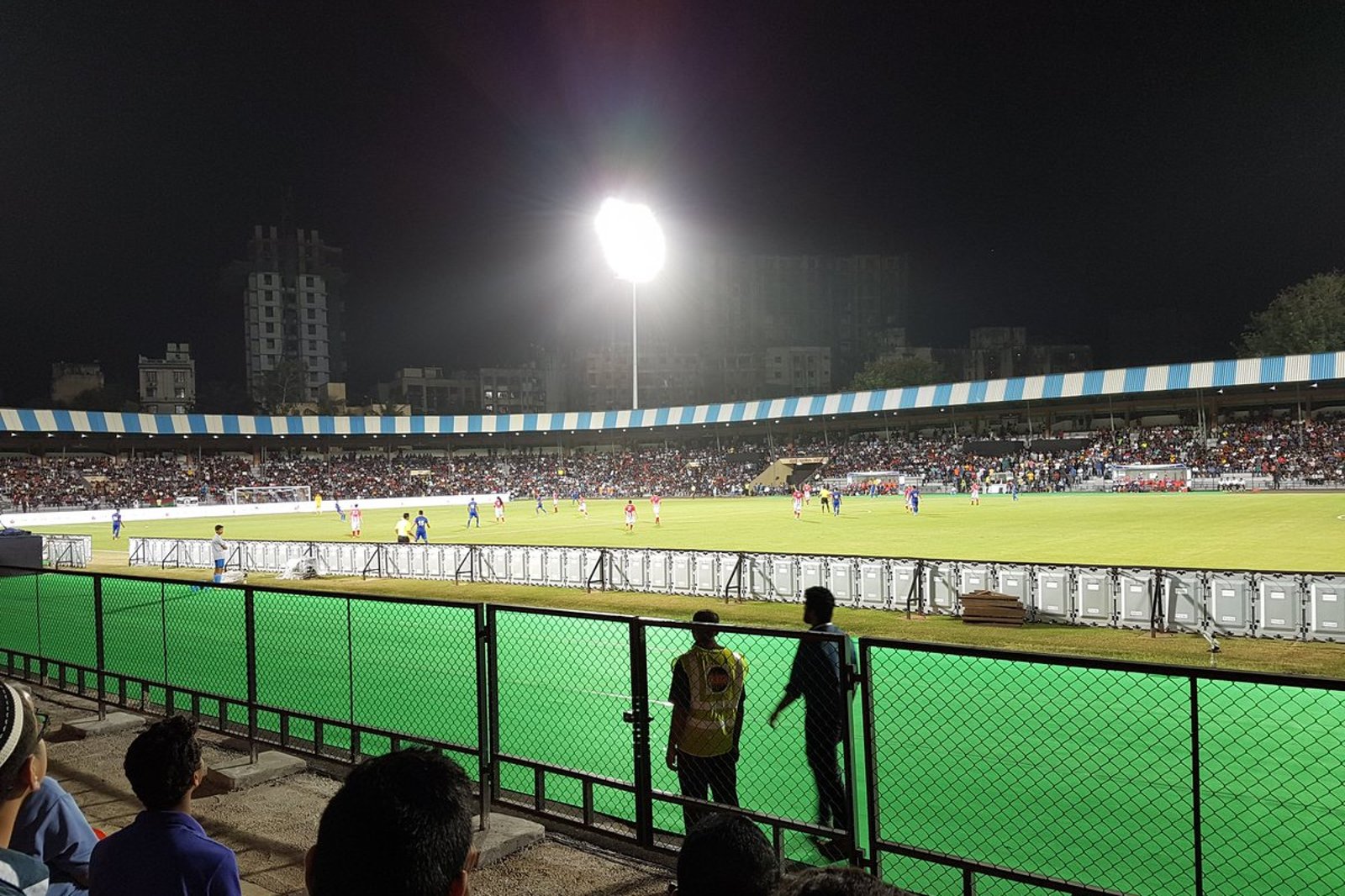 Floodlit football match with spectators in the stands at the Mumbai Football Arena at night