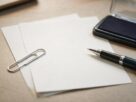 Two blank sheets of paper with a paperclip, a pen and a stamp pad on a desk