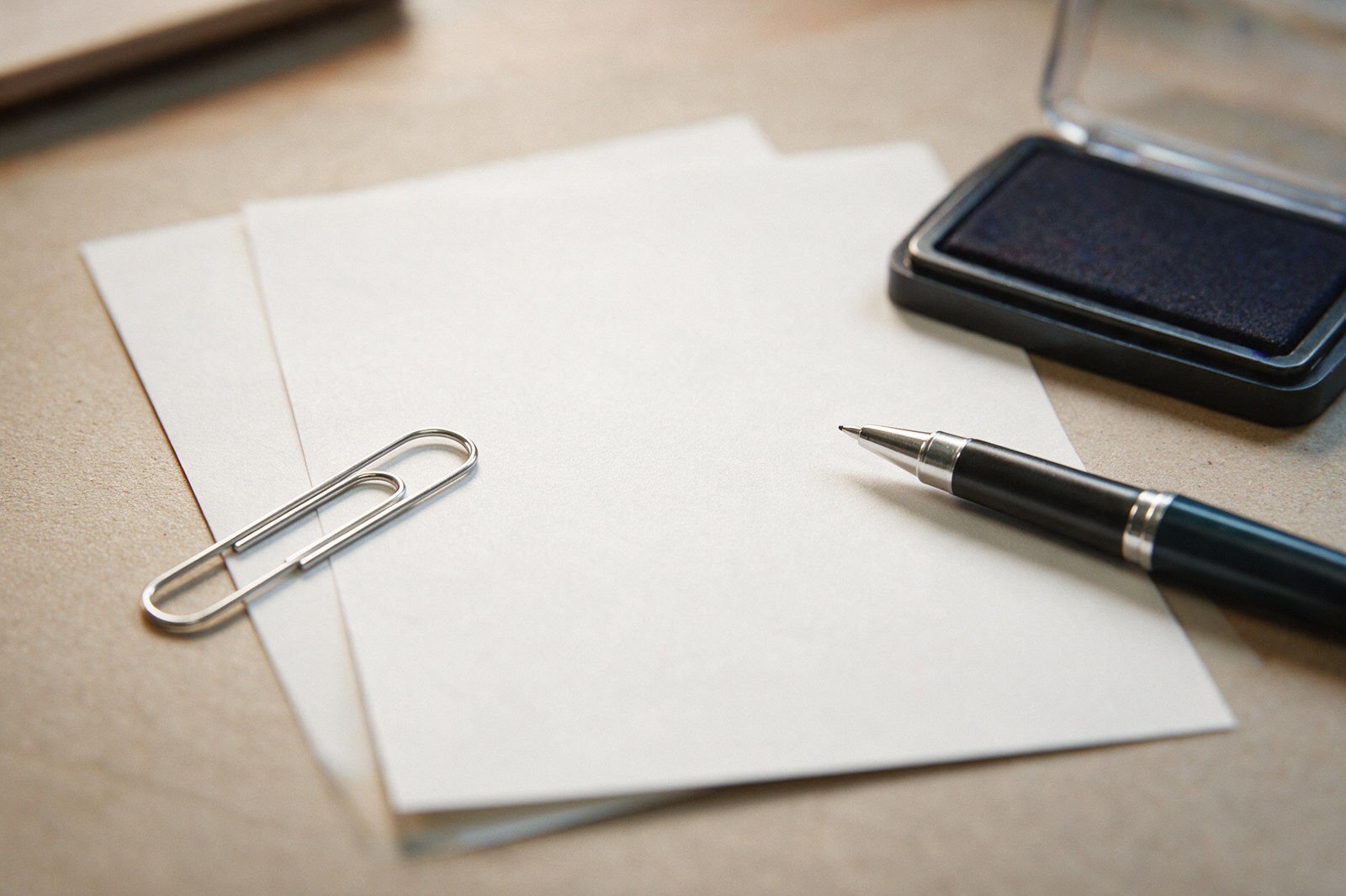 Two blank sheets of paper with a paperclip, a pen and a stamp pad on a desk