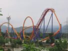 Red and blue steel roller coaster track with loops at Imagicaa, with green hills behind