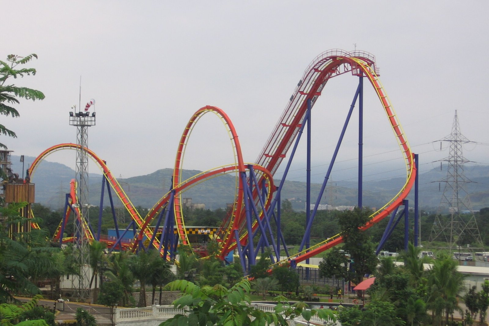 Red and blue steel roller coaster track with loops at Imagicaa, with green hills behind