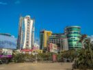 Tall apartment tower beside glass fronted commercial buildings and billboards under a clear blue sky in Vashi