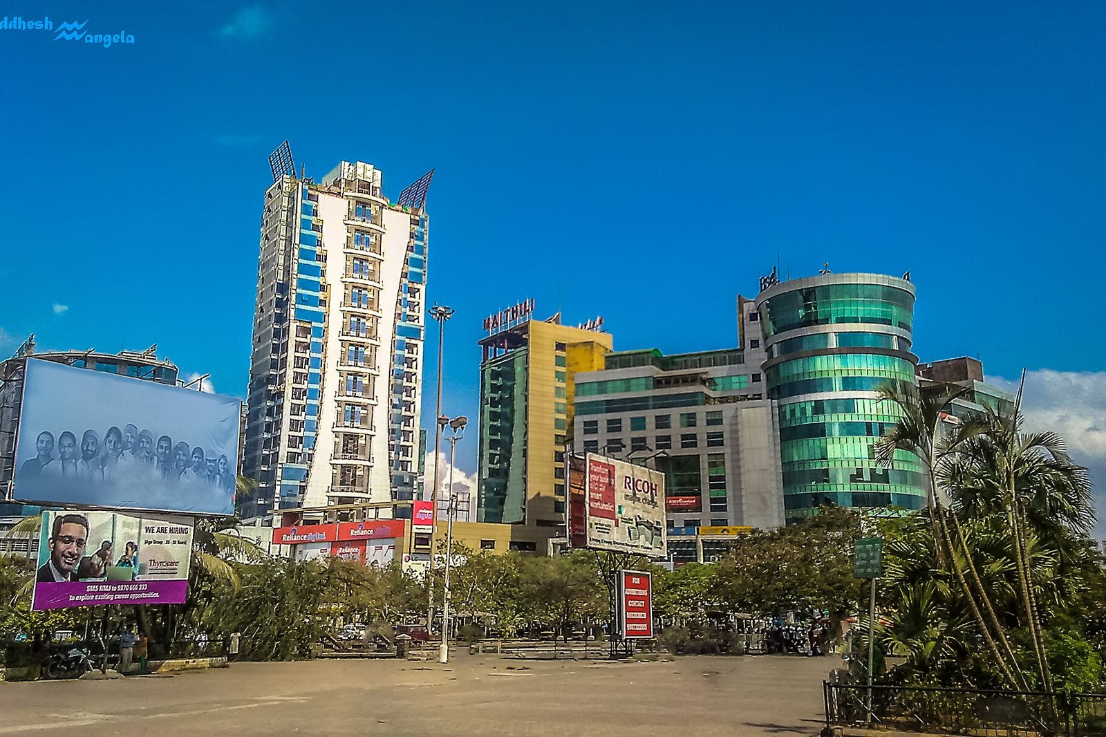 Tall apartment tower beside glass fronted commercial buildings and billboards under a clear blue sky in Vashi