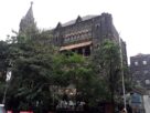 Dark stone Gothic Bombay High Court building with a church style spire, seen through trees in Mumbai