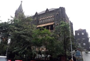 Dark stone Gothic Bombay High Court building with a church style spire, seen through trees in Mumbai