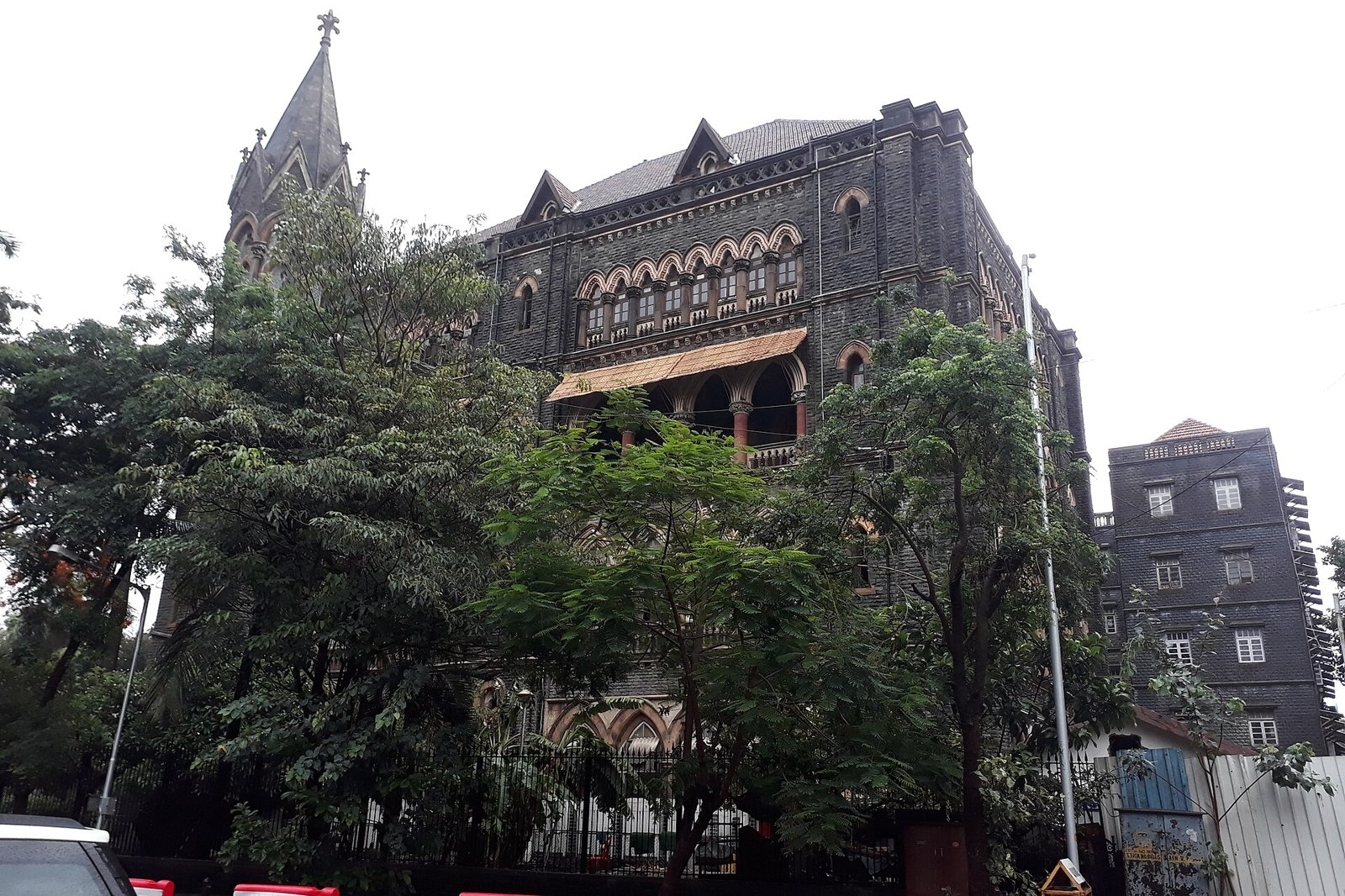 Dark stone Gothic Bombay High Court building with a church style spire, seen through trees in Mumbai