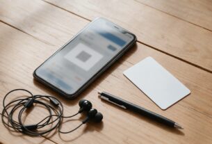 A smartphone with a blurred QR ticket screen, a blank card, earbuds and a pen on a desk, AI-generated illustrative render