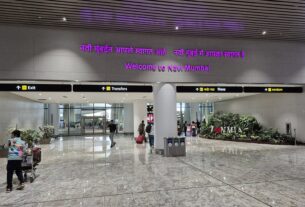 Arrivals area at Navi Mumbai International Airport with overhead signs for Exit and Transfers and a welcome message in Hindi, Marathi and English