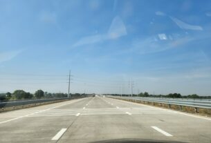 Six-lane concrete expressway with a truck ahead under a blue sky