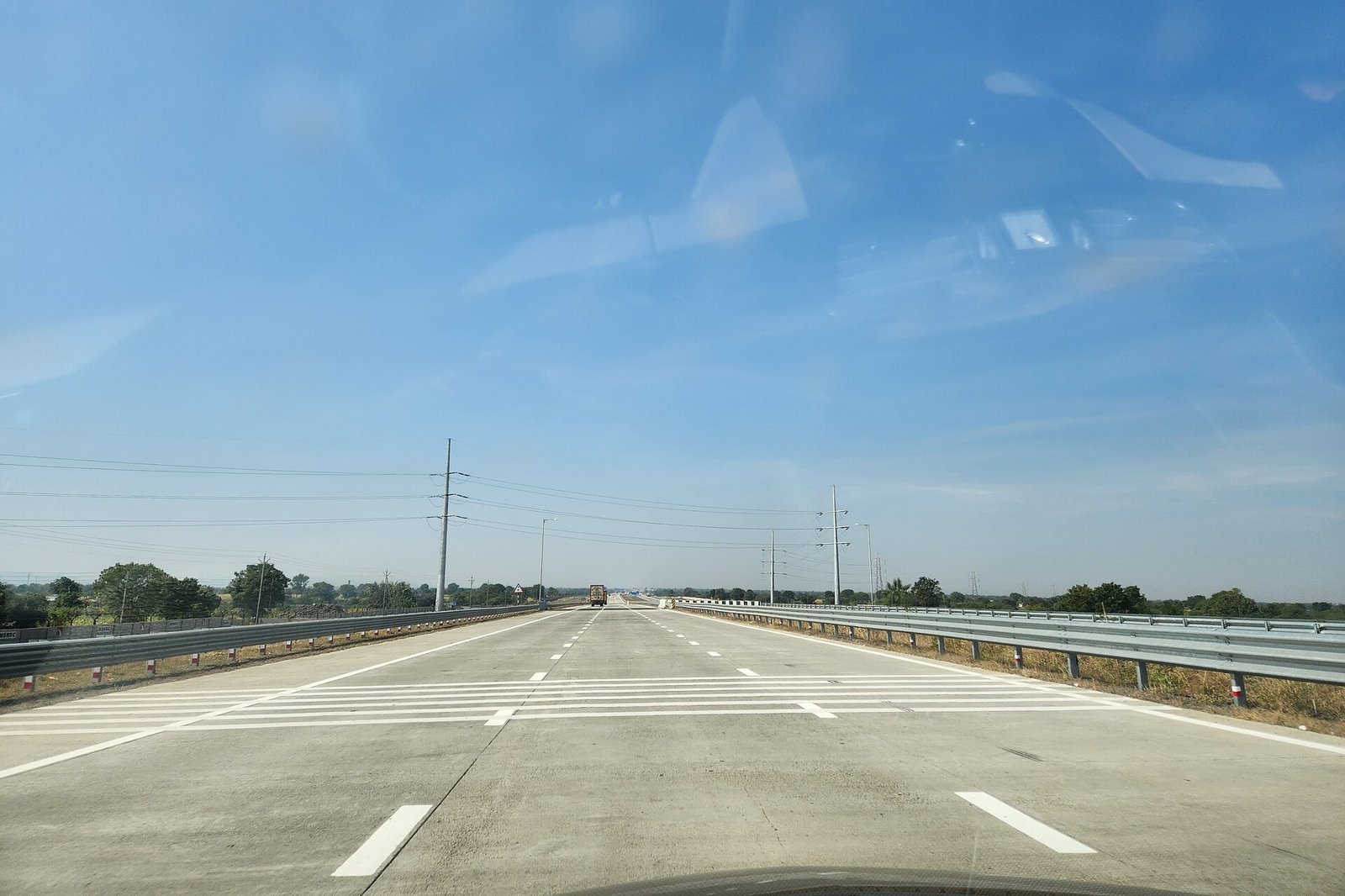 Six-lane concrete expressway with a truck ahead under a blue sky