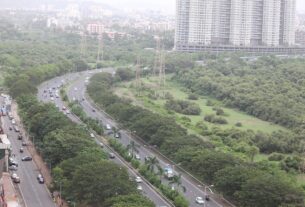 Palm Beach Road curving beside mangroves with cars on both carriageways and apartment towers behind in Navi Mumbai