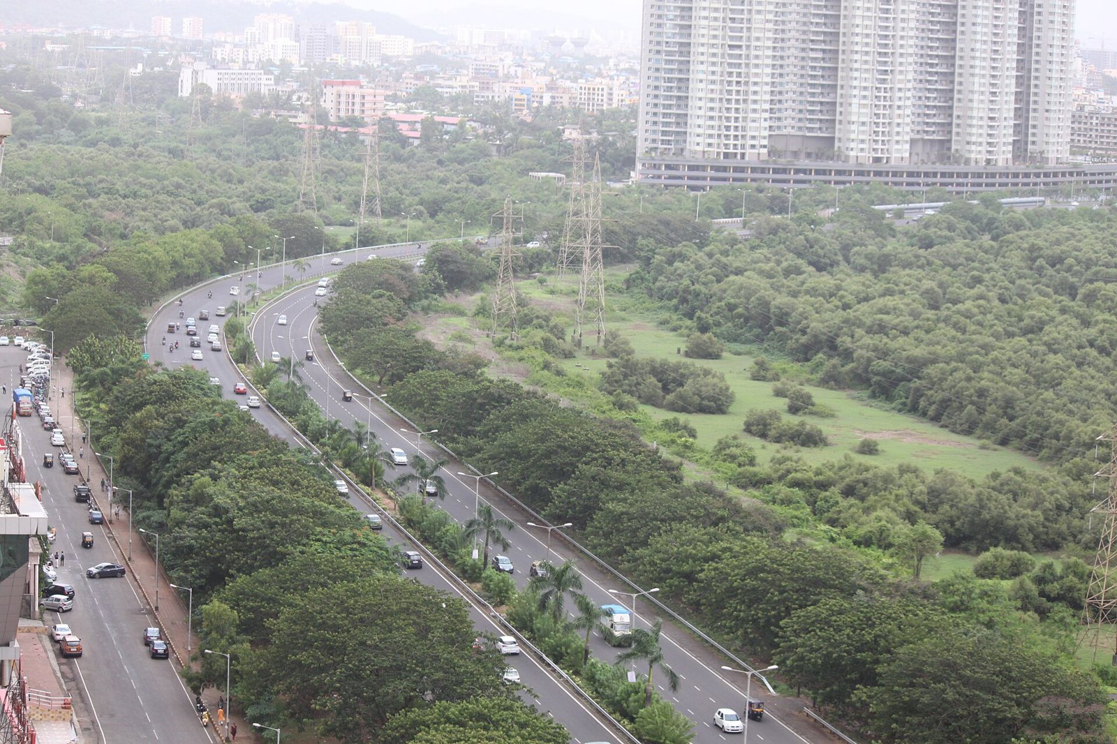 Palm Beach Road curving beside mangroves with cars on both carriageways and apartment towers behind in Navi Mumbai