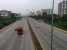 A wide multi lane highway with buses and cars passing apartment buildings and greenery along the Sion Panvel highway
