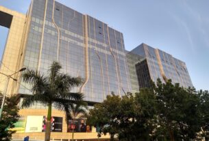Glass-fronted tower of the Seawoods Grand Central complex in Nerul with palm trees in front