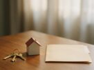 House keys, a small model house and a blank folder on a wooden table