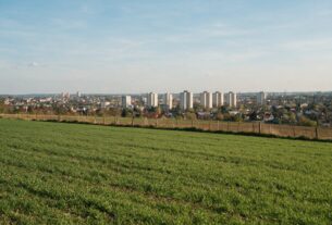 A green farm field with a fence at the edge of a growing city