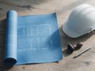 An architectural blueprint, a hard hat, a stamp and a pen arranged on a desk, AI-generated illustrative render