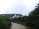White apartment buildings on a wooded hillside beside a brown stream in Kharghar