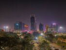 Tall buildings lit up at night in Vashi, seen over trees and a car park