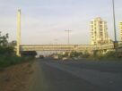 A cable stayed footbridge crossing a wide highway at Kharghar with apartment towers and trucks on the road