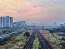 Railway tracks running past apartment towers and scrub under a hazy dawn sky near Seawoods in Navi Mumbai