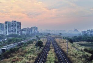 Railway tracks running past apartment towers and scrub under a hazy dawn sky near Seawoods in Navi Mumbai