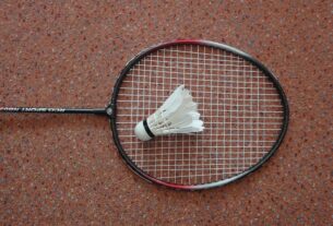 A badminton racket with a feather shuttlecock resting on its strings