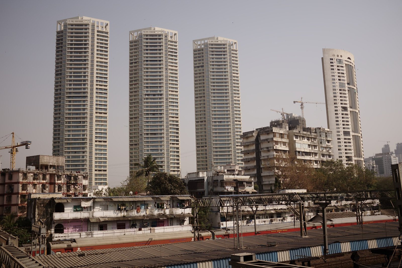 Four tall residential towers rising above older low-rise buildings and a railway line, with construction cranes on the skyline