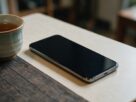 A smartphone with a dark screen lying on a table next to a cup of tea